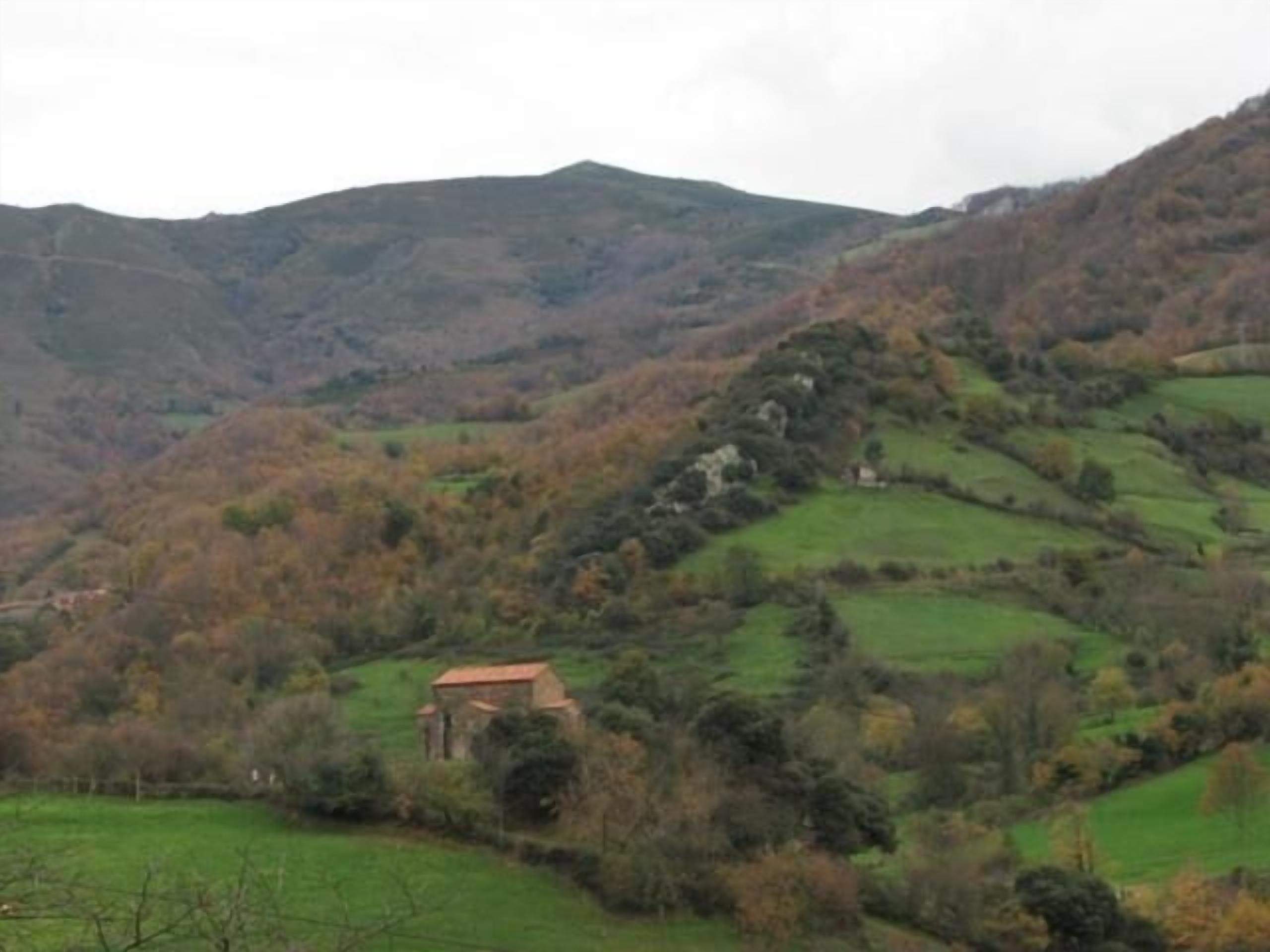 Paisaje rural con colinas onduladas, un pequeño edificio de piedra y árboles dispersos.