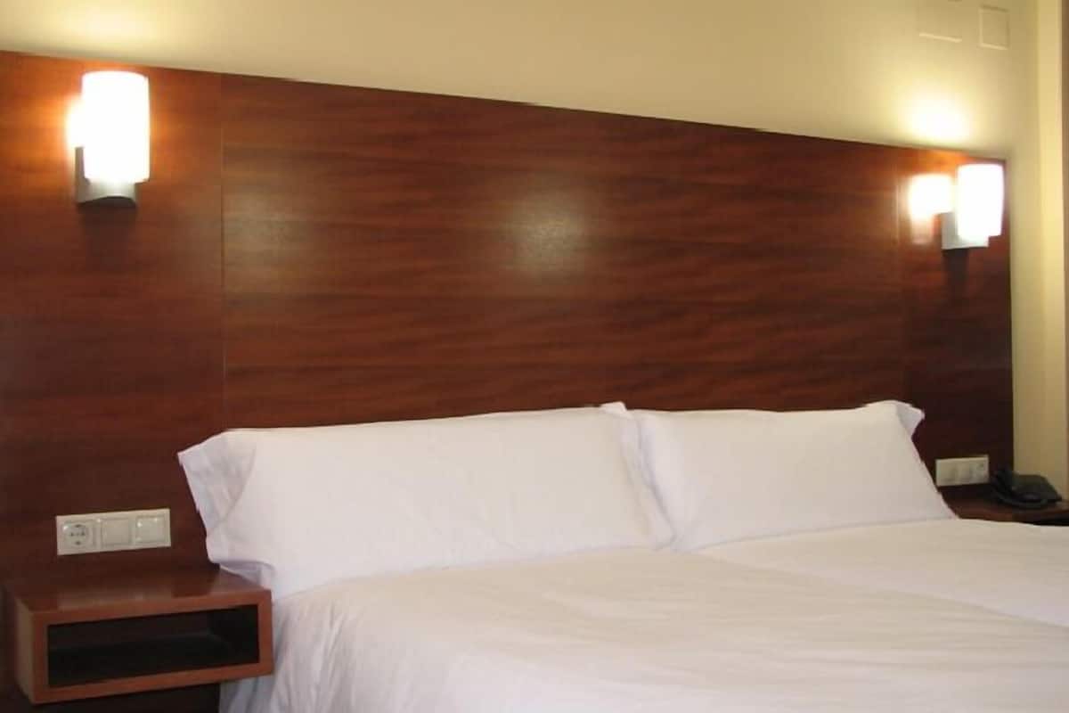 A hotel room with a wooden headboard, two white pillows, a bedside table with a phone, and a power outlet.