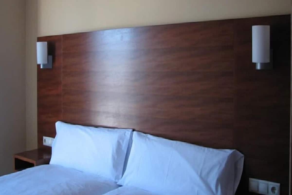 A hotel room with a wooden headboard, two bedside lamps, and a neatly made bed.