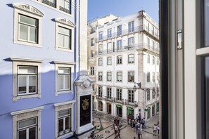 A view of a narrow street with buildings on either side, featuring balconies and large windows.