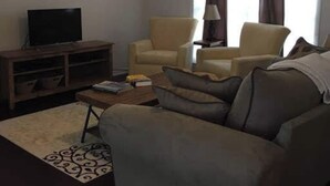 Una sala de estar con un sofá, dos sillones, una mesa de centro, un televisor y una lámpara.