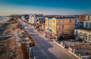 A coastal street lined with colorful buildings, a sandy beach, and a clear sky.