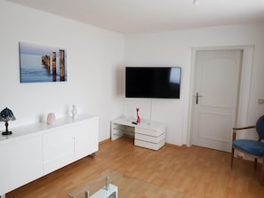 Un soggiorno moderno con un'unità TV bianca, una televisione a schermo piatto, una porta e una poltrona blu.