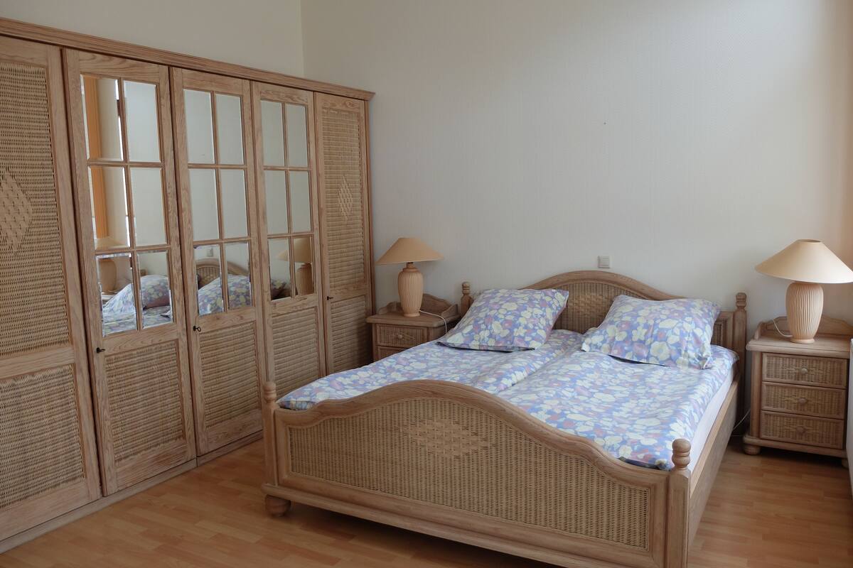 Ein Schlafzimmer mit einem Holzbett, zwei Nachttischen, einem Kleiderschrank und einem Spiegel.