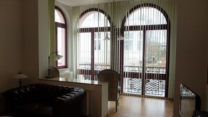 A room with a sofa, a desk, a chair, and large windows with a view of the outside. - Haus Lucie (Heringsdorf)