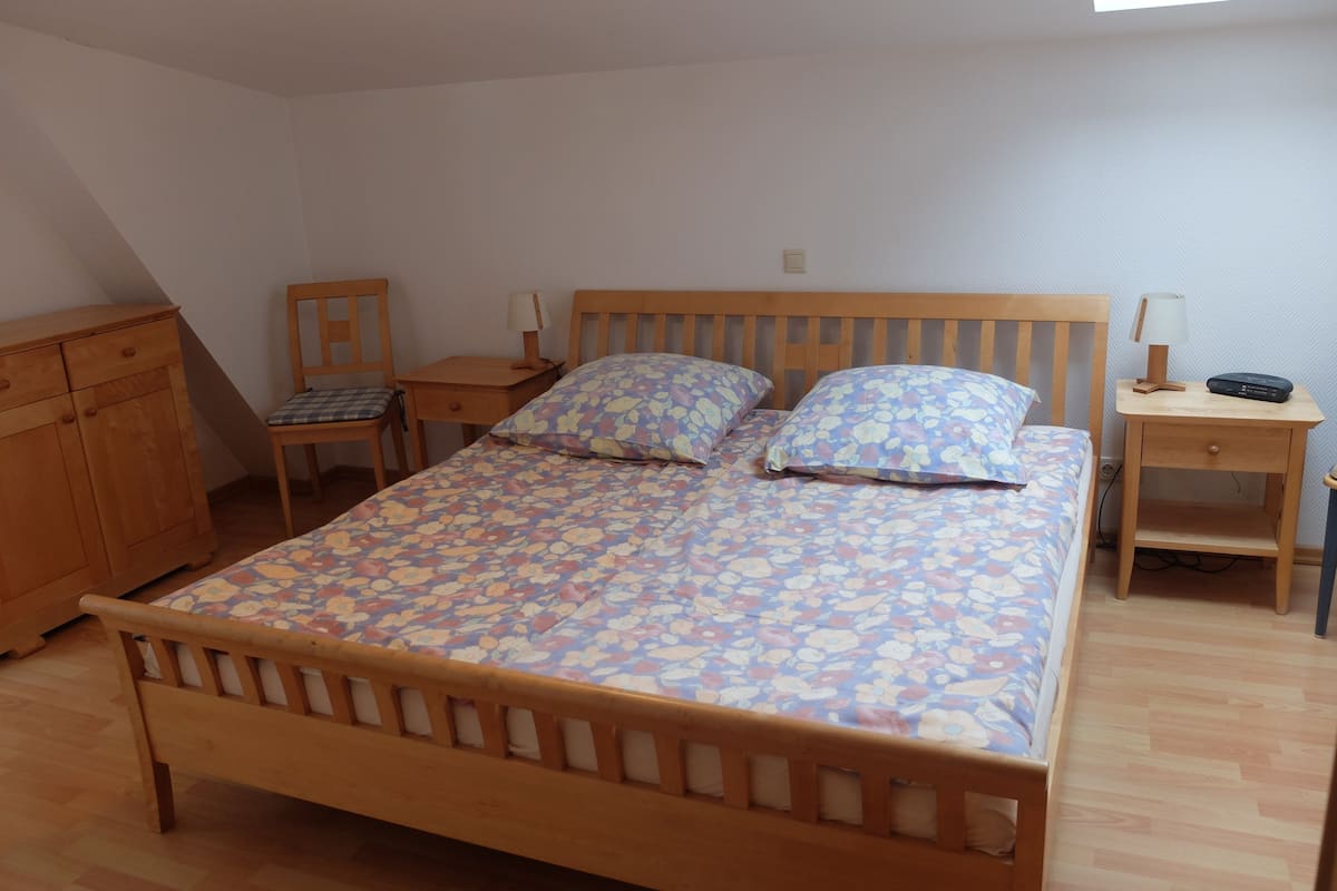 Ein Schlafzimmer mit einem hölzernen Bett, zwei Nachttischen, einem Sessel und einem Holzschrank.