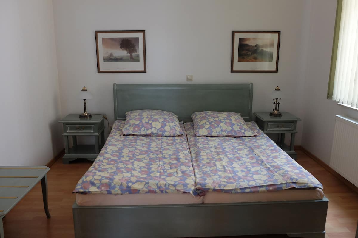 Ein Doppelbett mit Blumenmuster, zwei Nachttische mit Lampen sowie zwei gerahmte Bilder an der Wand.