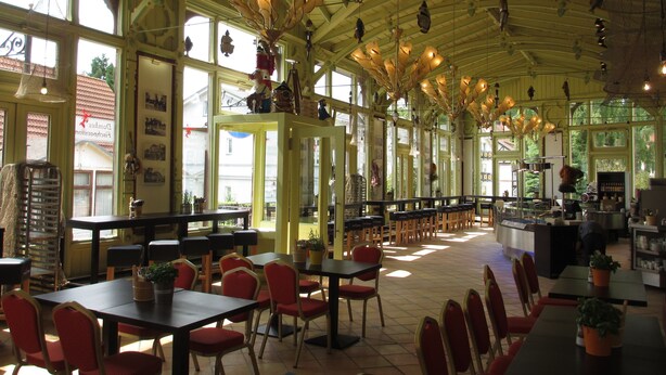 A spacious restaurant with high ceilings and large windows, featuring multiple tables and chairs arranged for dining. - Haus Lucie (Heringsdorf)