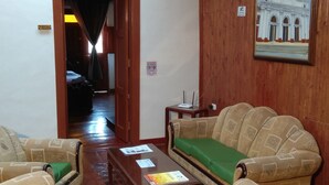 Una camera d'albergo con pavimento in legno, due divani decorati con cuscini verdi, un tavolino in legno e un quadro raffigurante un edificio.