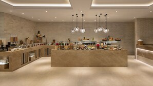 A modern breakfast bar with a variety of food items and beverages, a brick wall background, and pendant lighting. - Lemon Tree Premier New Town Kolkata (Barasat)