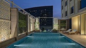 A swimming pool with a tiled floor, surrounded by walls with geometric patterns and greenery. - Lemon Tree Premier New Town Kolkata (Barasat)