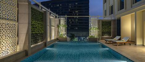 A swimming pool with a tiled floor, surrounded by walls with geometric patterns and greenery.