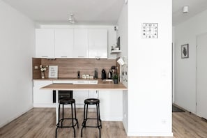 A modern kitchen with white cabinets, a wooden countertop, and two black stools. - M&R Apartament Airport&Business Komputerowa (Warsaw)