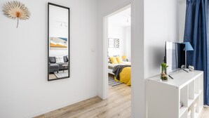 Una habitación moderna y luminosa, con piso de madera, una consola blanca, un espejo grande y una cama con ropa de cama amarilla.