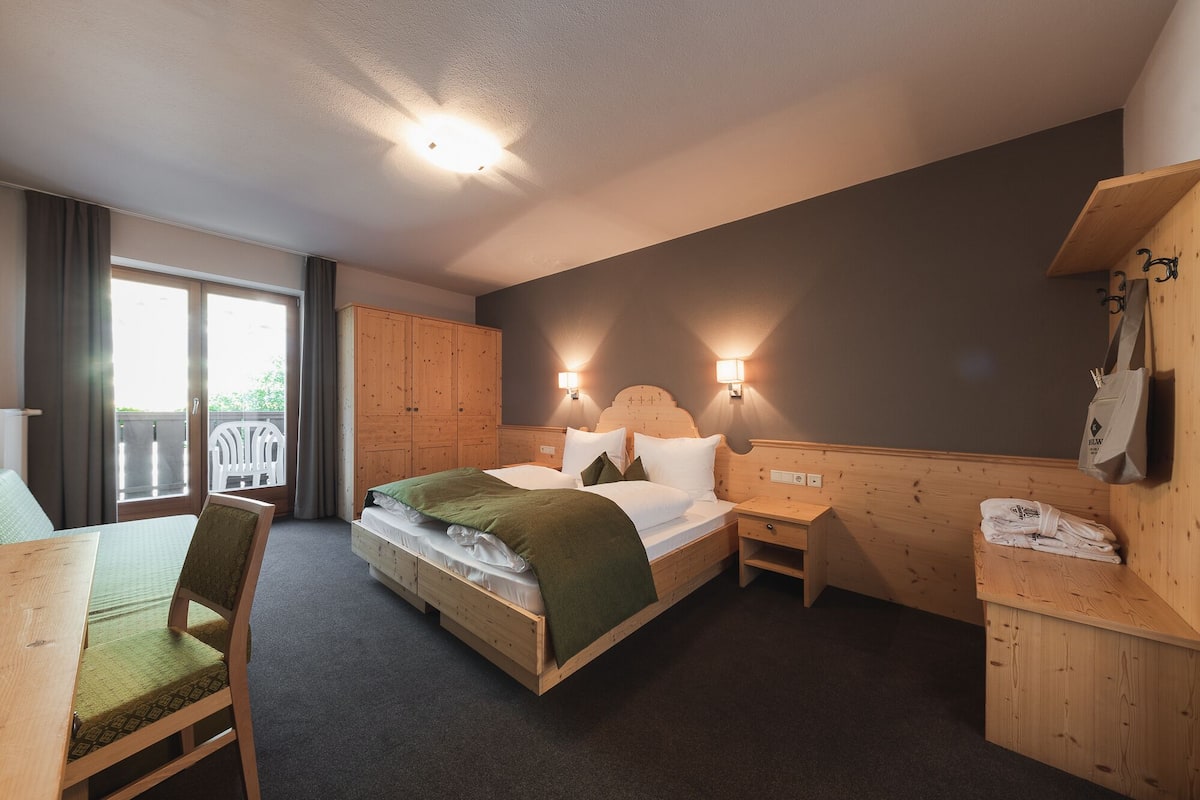 A hotel room with a bed, a desk, a chair, a wardrobe, and a balcony.