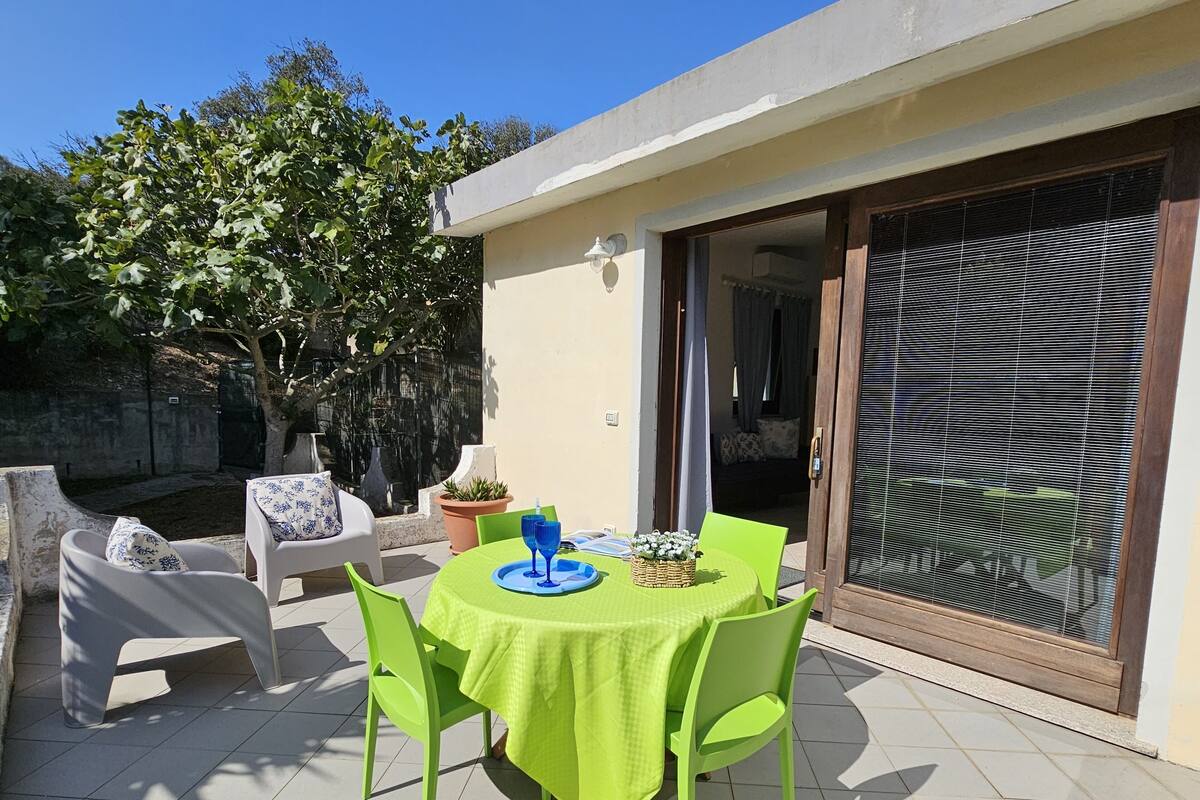 A patio with a table set for two, surrounded by chairs, a potted plant, and a window with blinds.