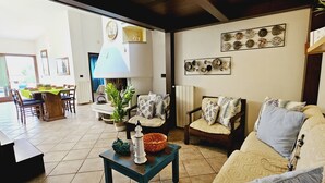 A living room with a sofa, chairs, a table, and decorative items. There is a dining area in the background with a table and chairs. - Le Villette di Ruoni (Santa Teresa di Gallura)