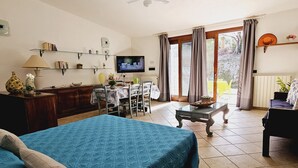 A well-lit room with a bed, a dining table, and a TV. - Le Villette di Ruoni (Santa Teresa di Gallura)
