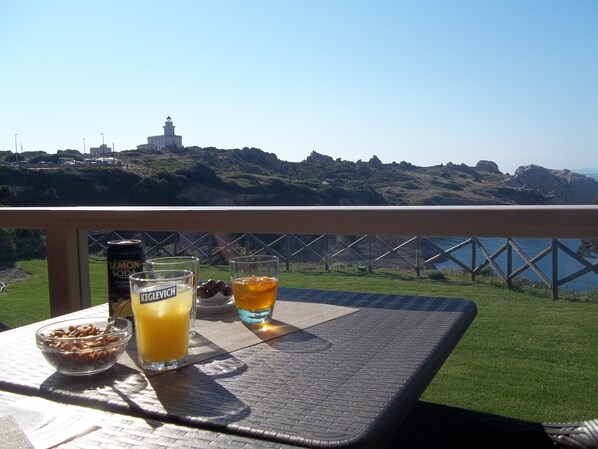 Una mesa con un tazón de cereal, una lata de refresco de limón y dos vasos de bebidas, con vistas a un paisaje costero y un faro.