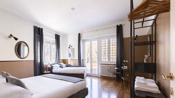 Une chambre d’hôtel avec deux lits, une grande fenêtre, un radiateur, une chaise et une étagère avec des serviettes.