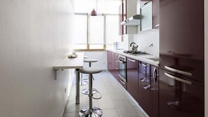 Une cuisine compacte dotée d’un plan de travail blanc, d’appareils électroménagers en acier inoxydable et d’une fenêtre laissant entrer la lumière naturelle.