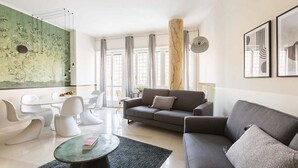 Un salon moderne avec un canapé gris, des fauteuils blancs, une table basse ronde et un grand tableau abstrait accroché au mur.