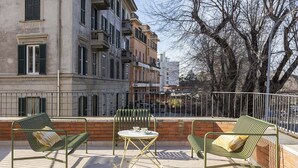Un espace extérieur aménagé avec deux chaises en métal vert et une petite table ronde, le tout adossé à un mur de briques et à une rambarde en métal.
