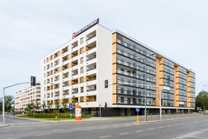 Un hotel moderno de varios pisos con un llamativo letrero de "DOM DEVELOPMENT", con balcones, fachada de vidrio y un patio central con vegetación.