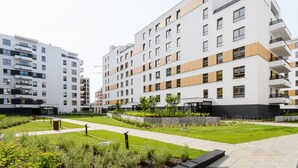 A modern apartment building with multiple floors, balconies, and a well-maintained garden area with pathways and greenery. - M&R Apartament Airport&Business DeLuxe Cybernetyki (Warsaw)