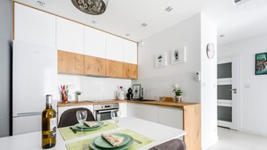 A modern kitchen with white cabinets, a wooden countertop, and a dining area with a table set for two. - M&R Apartament Airport&Business DeLuxe Cybernetyki (Warsaw)