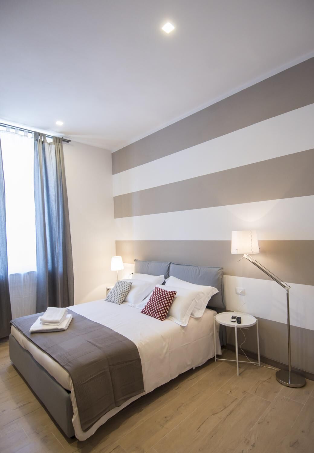 Een moderne hotelkamer met een groot bed, nachtkastje, vloerlamp en uitzicht op het groen buiten.