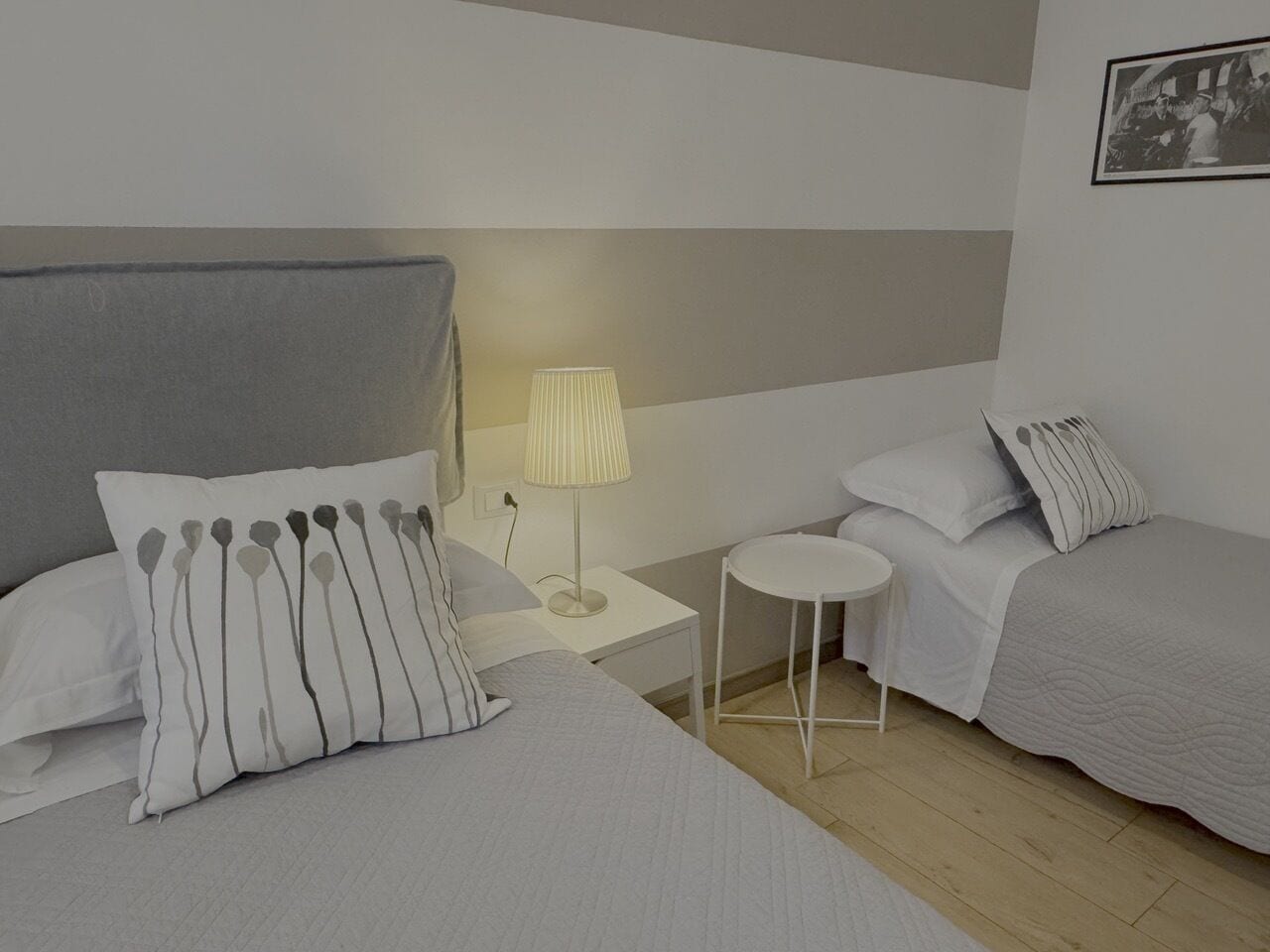 A hotel room with two beds, a bedside table with a lamp, and a small round table.