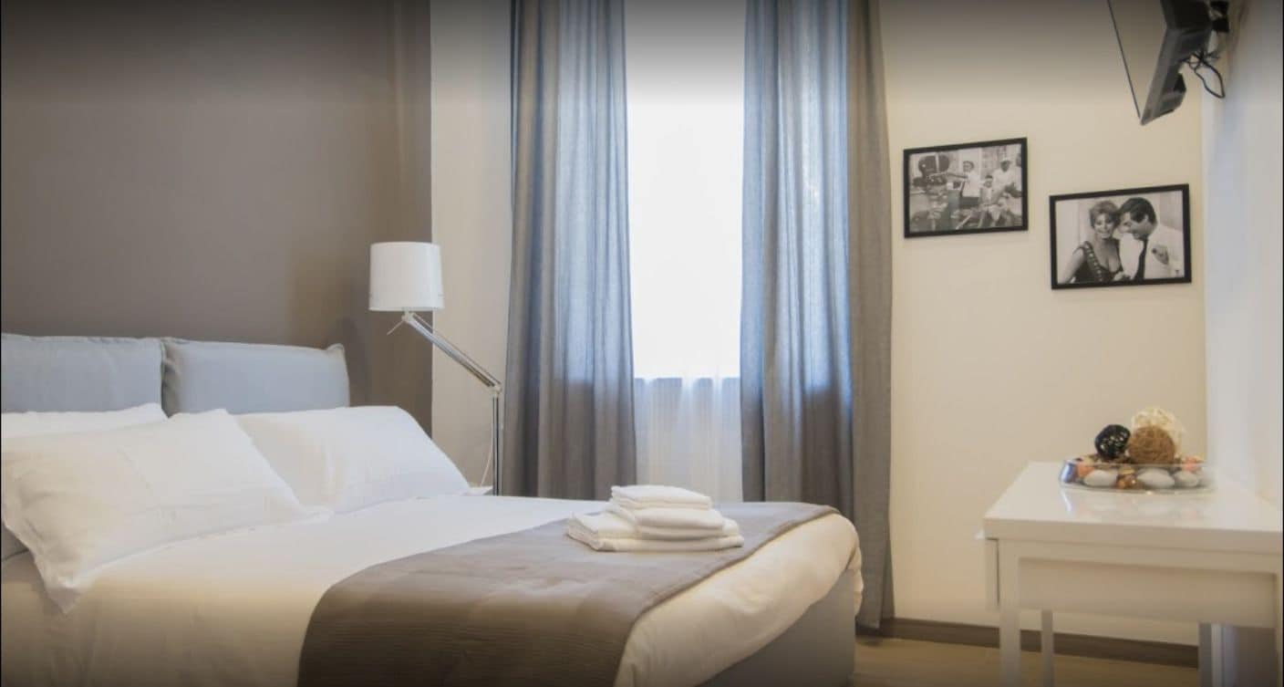 Una habitación de hotel con cama, una mesita de noche con lámpara y dos cuadros en la pared.