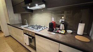 Cocina moderna con estufa a gas, cafetera y hervidor. Cuenta con encimera de madera y horno empotrado.