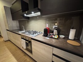 Cocina moderna con estufa a gas, cafetera y hervidor. Cuenta con encimera de madera y horno empotrado.