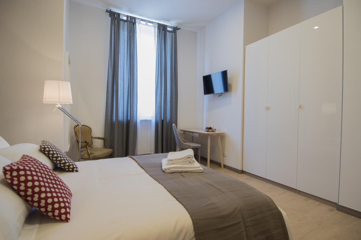 A hotel room with a bed, a desk, a chair, a TV, and a wardrobe.