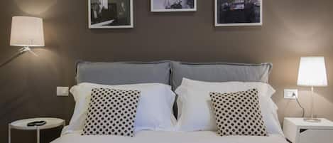 A neatly made bed with white and gray bedding, two bedside tables with lamps, and three framed photographs on the wall.
