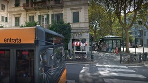 Un autobús con la leyenda "entrata" en una parada de autobús, con un edificio al fondo.