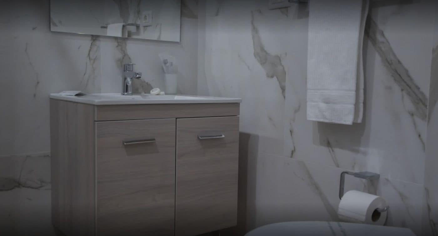 Ein Badezimmer mit Marmorwand, einem Holzkosmetikschrank mit zwei Schubladen, einem Spiegel und einem Toilettenpapierhalter.