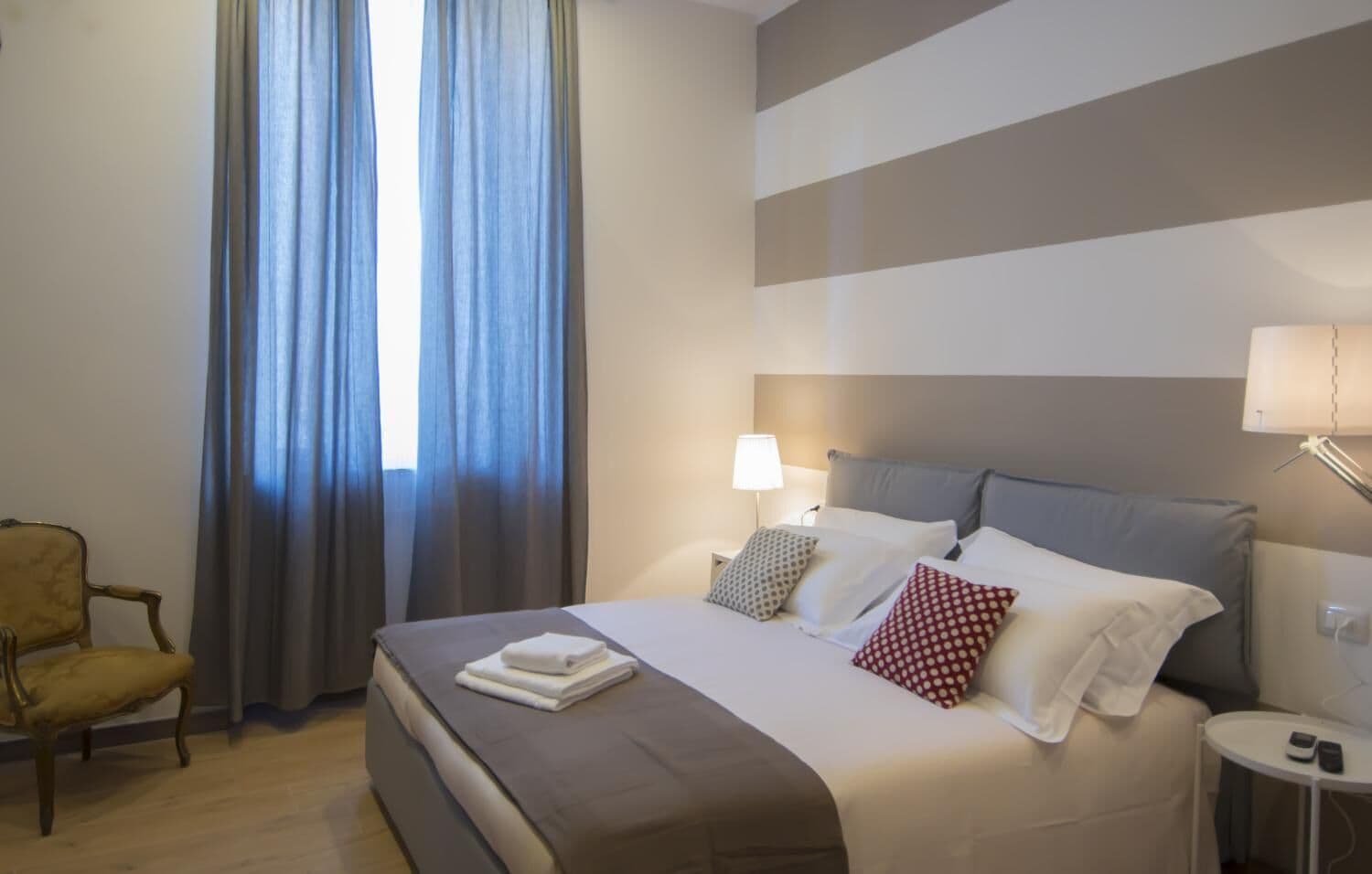 Una habitació d'hotel amb un llit, una cadira i cortines.