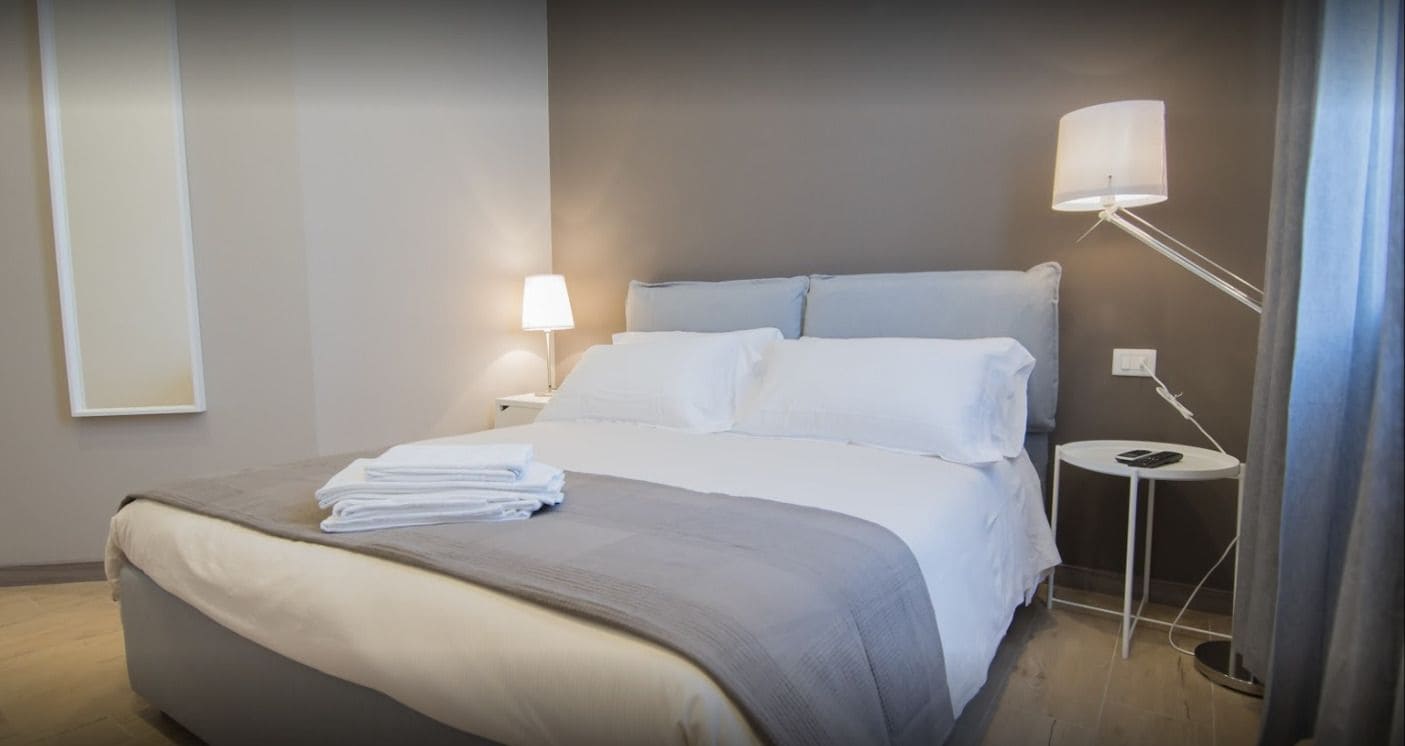 A neatly made bed with a folded towel, a bedside lamp, and a small table with a phone.