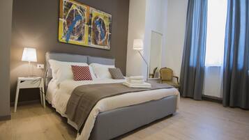 A modern hotel room with a large bed, two bedside lamps, a chair, a large window with curtains, and a colorful abstract painting on the wall.