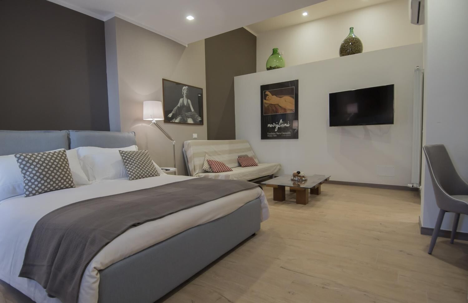 Quarto de hotel moderno com uma cama grande, um sofá, uma mesa de centro e uma televisão.