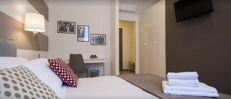 A hotel room with a bed, a desk, and a TV mounted on the wall.