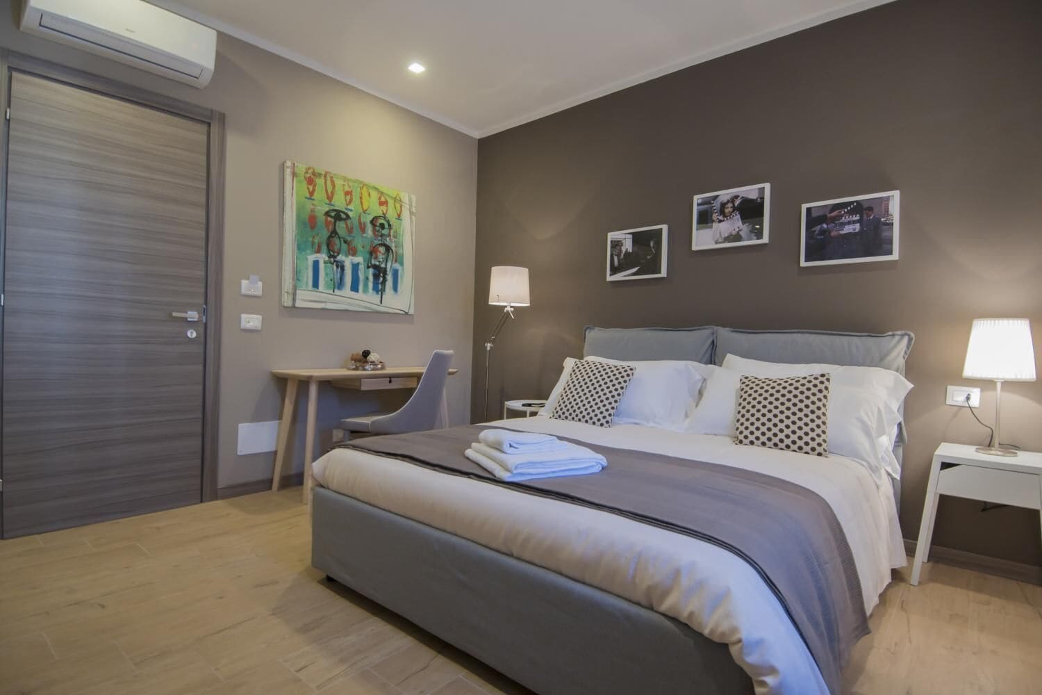 Une chambre avec un grand lit, un bureau et une chaise. Il y a trois tableaux encadrés accrochés au mur.