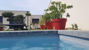 A swimming pool with a concrete edge, surrounded by potted plants and a building with a flat roof. - Contemporary villa at the door of the luberon (morieres les avignon)