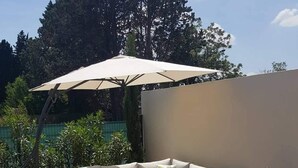 A patio with a beige sectional sofa, a wooden coffee table, a patterned rug, a red potted plant, and a large umbrella. - Contemporary villa at the door of the luberon (morieres les avignon)