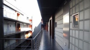 A corridor with a metal railing, a tiled floor, and a wall with a window.