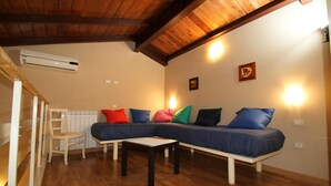 A cozy living room with a wooden ceiling, a sectional sofa with colorful cushions, a wooden chair, and a small table. - La Chioccia (Valmontone)