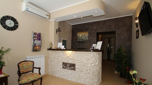 A reception area with a stone-textured counter, a clock, and a chair with a colorful cushion. - La Chioccia (Valmontone)